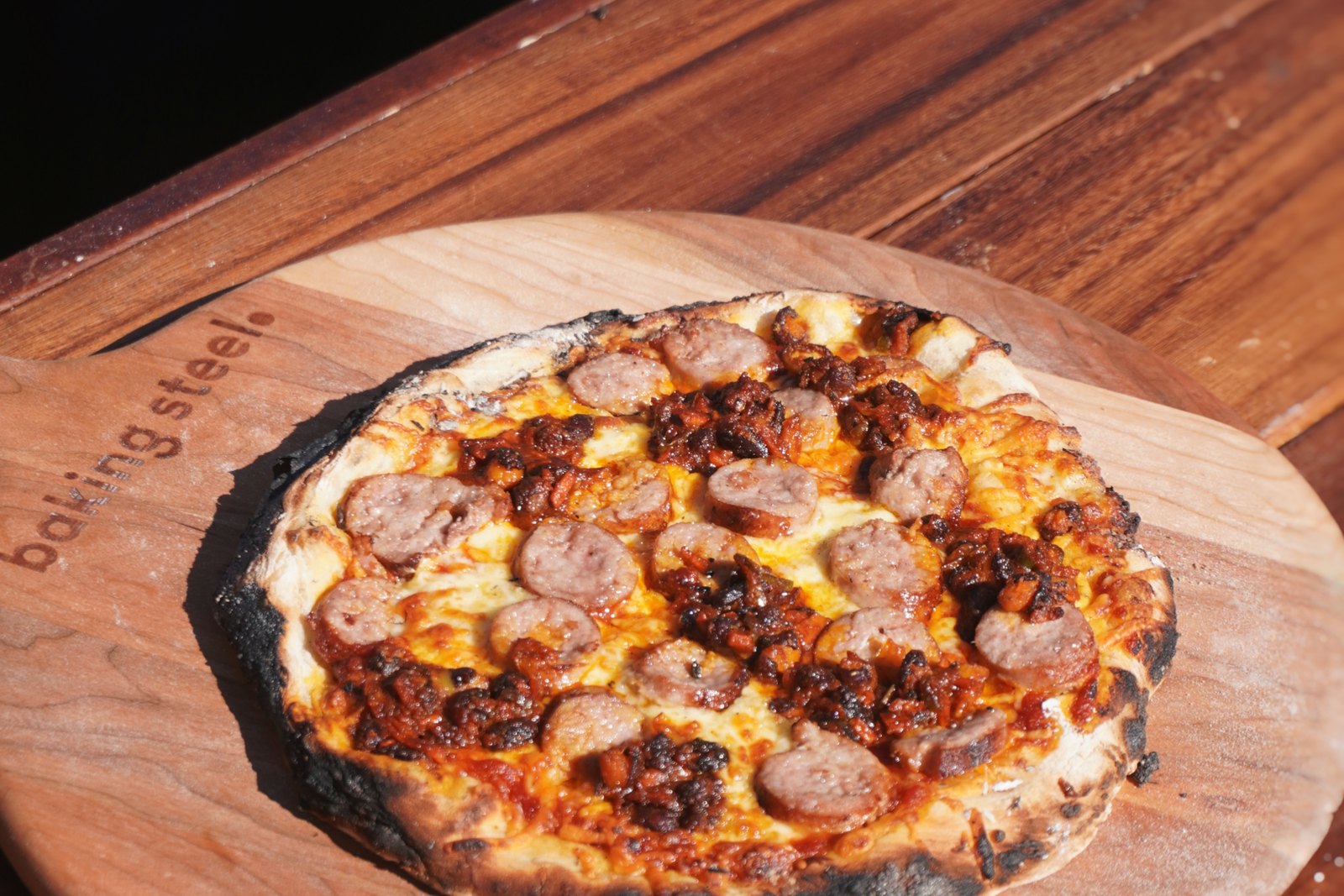 A finished boerewors pizza on a Baking Steel peel, cooked over an open fire in the bush