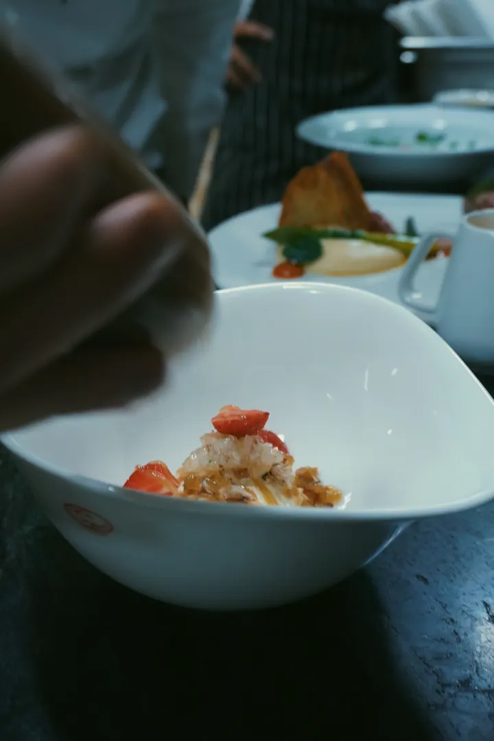 A cook finishing a dish in a white bowl at the pass in Bengaluru
