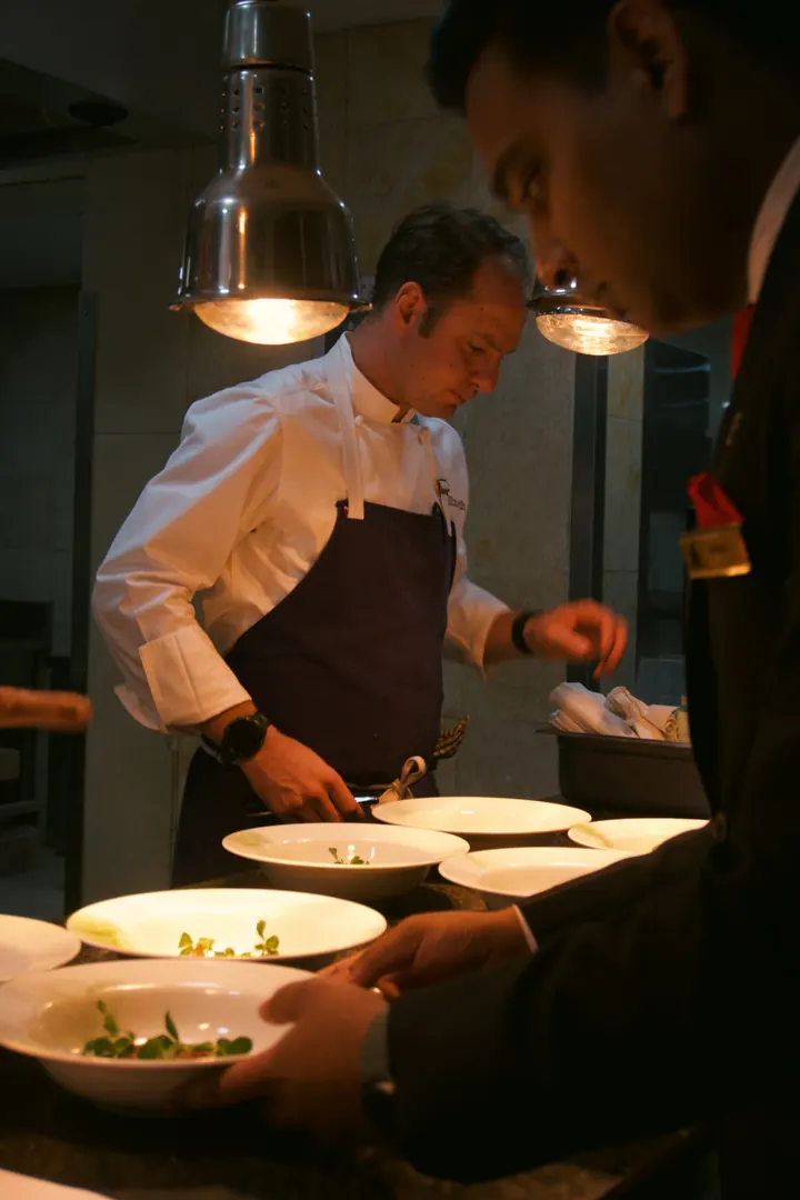 Chefs working together under heat lamps at the kitchen pass in Bengaluru