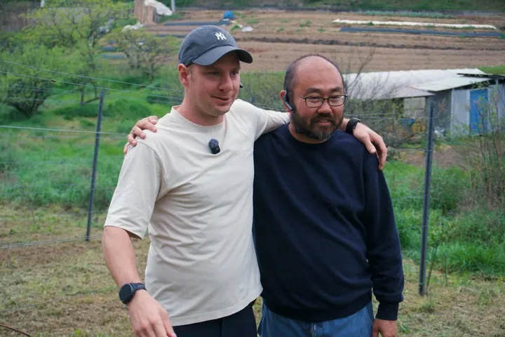 Two men standing together with an arm around one another beside the vines
