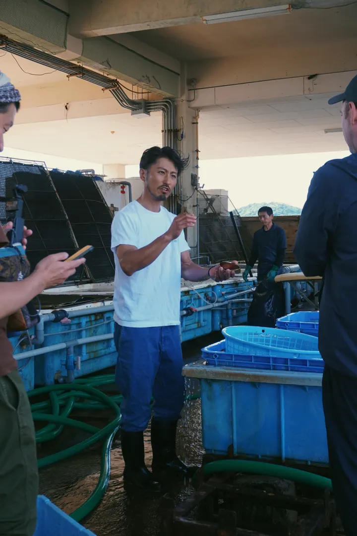 A man holding a shellfish while explaining it to visitors beside blue tanks