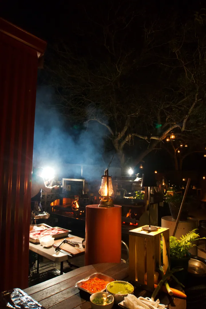 Food and serving dishes under warm lights beside an outdoor fire at Kruger Shalati