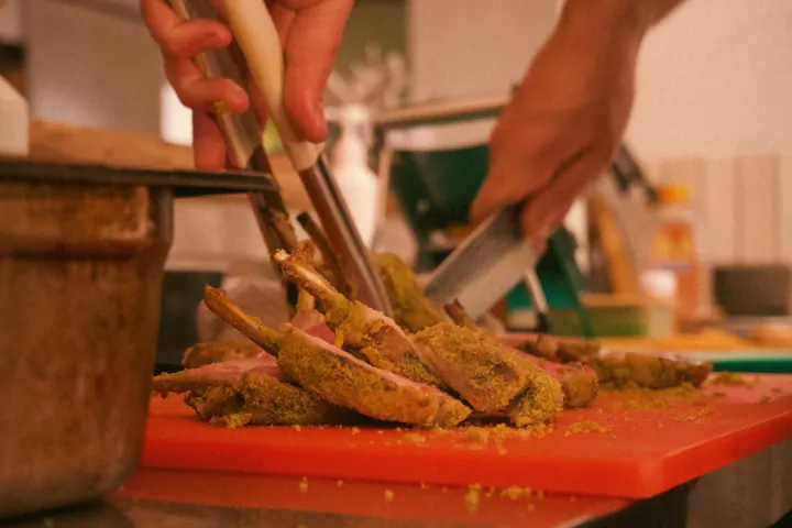 Hands carving cooked meat on a board in the kitchen at Few & Far