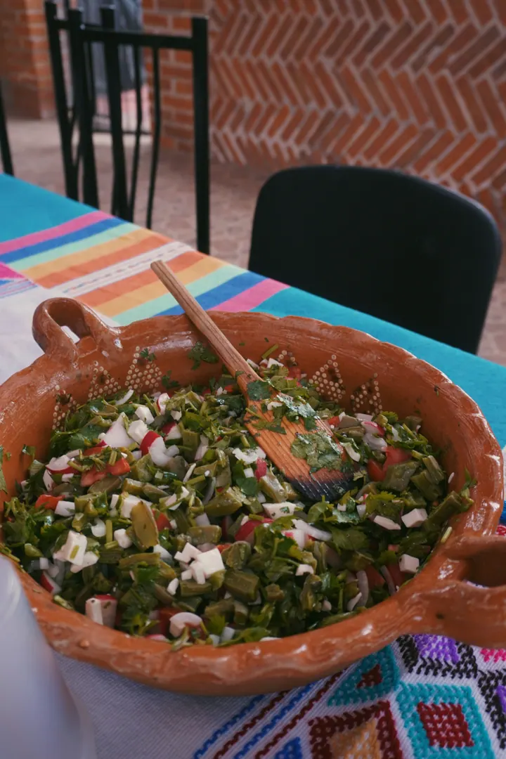 A clay bowl of chopped cactus salad on a brightly striped tablecloth