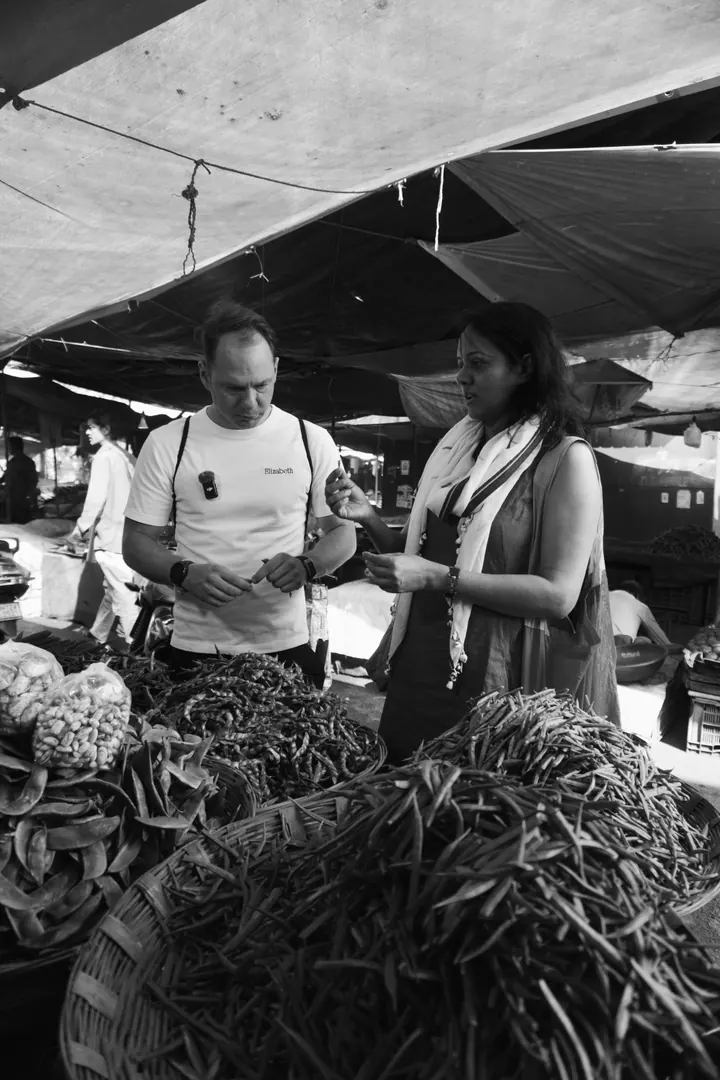 Two people examining ingredients beside baskets of vegetables at a Pune market