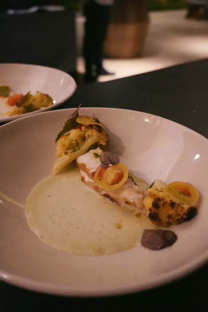 A plated dish with sauce, vegetables and herbs at Cap Karoso